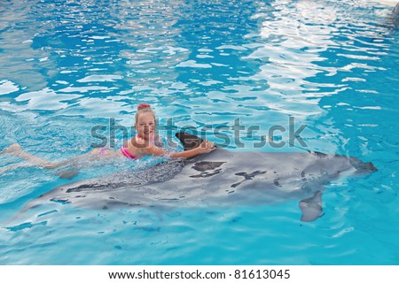 Smiling Girl Swimming with the Dolphin in the Swimming Pool