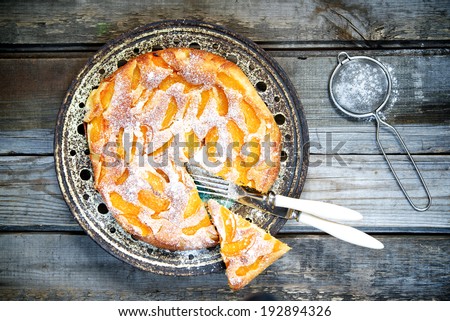 Cake with peaches, sprinkled with powdered sugar on a wooden table. top view