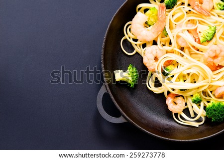 Pasta with prawns and broccoli in a frying pan on a black background