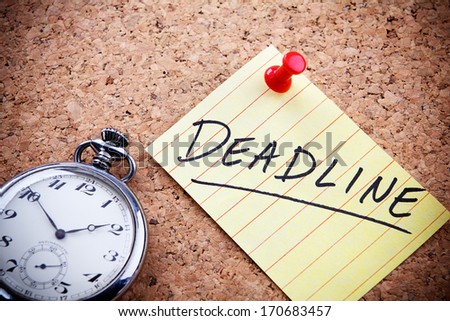 Deadline word written on a post note and hanged on the cork-board with an old pocket watch.