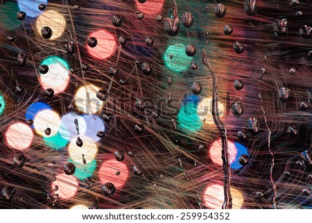 Abstract background made of scratched plastic with raindrops and distant blurry lights.