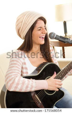girl with cap playing a guitar and singing on microphone
