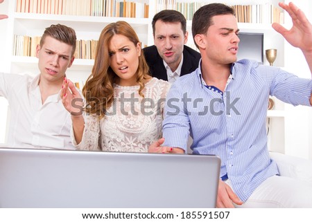 young frustrated casual group of friends sitting on couch looking at laptop, pissed off friends, cheering on computer