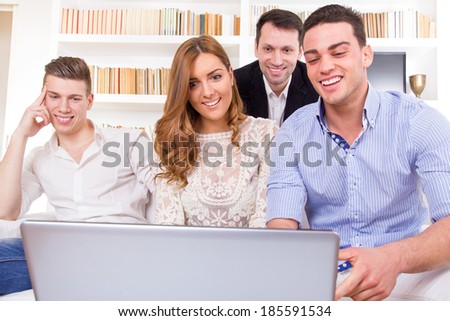 young happy casual group of friends sitting on couch looking at laptop