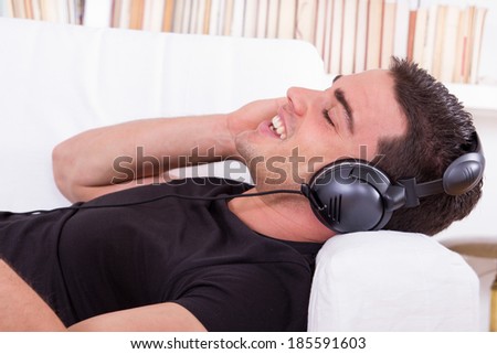 handsome man resting on couch listening to music with headphones and singing