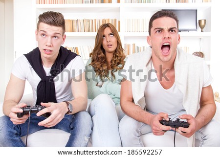 pretty bored women between two casual men playing video game with joystick