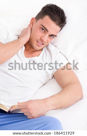 handsome man with neck pain reading book in bed wearing pajamas