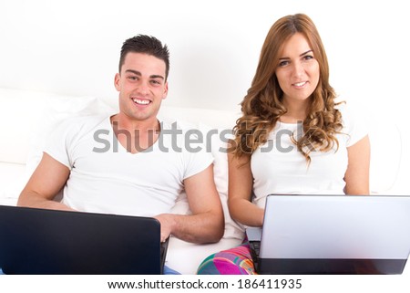 smiling couple with two laptop computers in bed. Man and woman both with computer. Young modern casual couple in bed. Caucasian man and woman. domestic happy image.