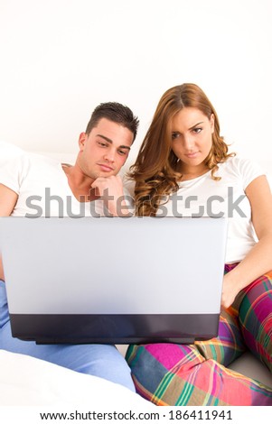 casual young happy couple enjoying using laptop computer in bed for the internet and watching movies