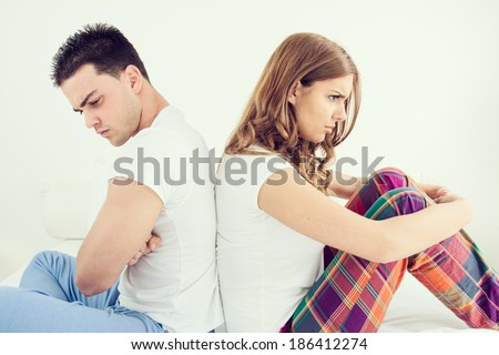 Upset young couple having marital problems or a disagreement sitting side by side in bed facing in opposite directions and ignoring one another. Caucasian man and woman in domestic bedroom atmosphere