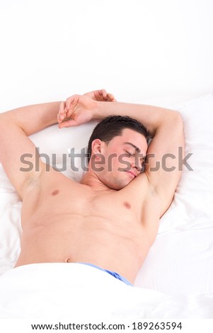 Image of handsome young half naked man with both hands up on pillow sleeping in bed