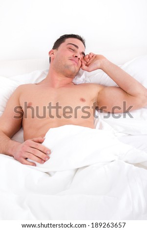 Young casual cheerful half naked man waking up in the bedroom and stretches in bed,  domestic atmosphere