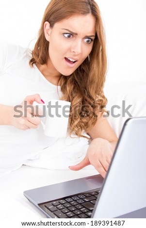 surprised worried woman looking in screen of laptop computer getting bad information while drinking coffee
