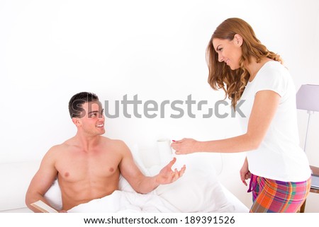 wife giving husband coffee in bed; beautiful young couple in love in bedroom with coffee in the morning