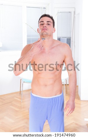 man using razor for shaving his beard and face, handsome man with naked torso shaving in pajamas