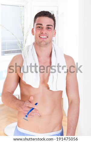 handsome guy with razor in hand after shaving smiling wearing towel around his neck