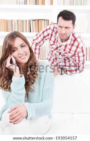 jealous worried man peering over the shoulder of his girlfriend while she is talking on the phone smiling
