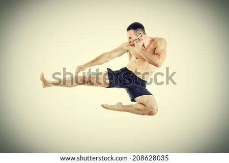 Determined muscular fighter performing professional flying kick in full length portrait
