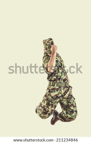 unknown soldier with hidden face in green camouflage uniform jumping up in air with fist sign of success