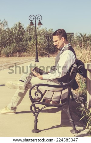 man in suit with glasses and whiskers reading book in the old town while sitting on bench, vintage and retro effect in picture