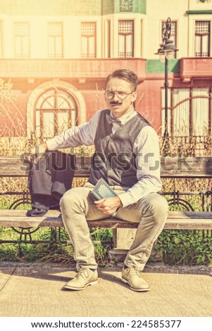 man in suit with glasses and whiskers holding book in the old town while sitting on bench in park posing, vintage and retro effect in picture