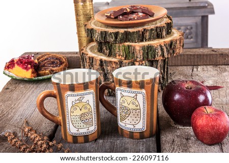 two empty cups for tea on retro wooden table next to the bark of a tree with an red apples next to
