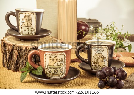 three retro empty cups for tea on retro wooden table next to the bark of a tree with cookies, white flower  and grape next to