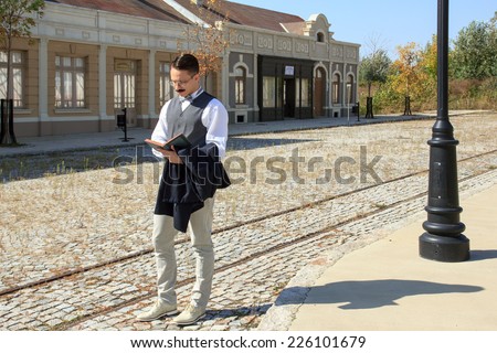 Man with mustache walking along the rails reading book wering vest in the old days of vintage city