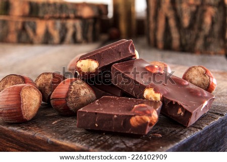 close up of stack of delicious milk chocolate pieces with hazelnuts on wooden table, retro style