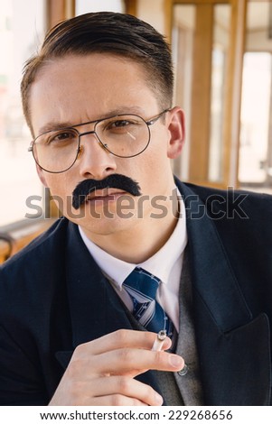 photo of man with glasses and whiskers  in a suit sitting in an old wooden wagon train and smoking a cigar, retro vintage fashion style