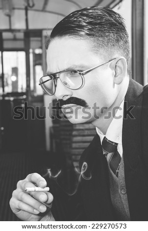 black  and white photo of man with glasses and whiskers  in a suit sitting in an old wooden wagon train and smoking a cigar, retro vintage fashion style