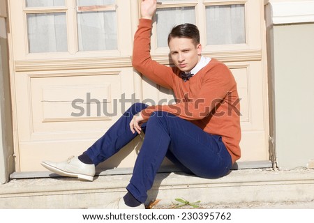 young man in sweater sitting on steps in front of house and posing , vintage retro photo