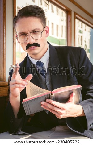 photo of man with glasses and whiskers  in suit sitting in an old wooden wagon train and smoking cigar while reading book , retro vintage fashion style