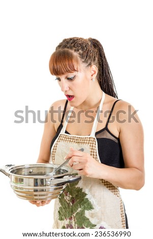 Surprised woman in the kitchen stirring the pot looking at burnt food , Inexperienced cook in apron holding pot and spoon looking shocked