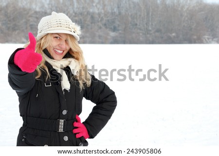 winter happy woman in snow looking up at camera with thumb up, copy space outside on snowing cold winter day. Portrait Caucasian smiling female model with pink gloves in first snow
