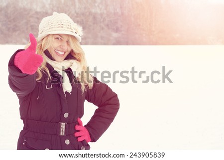 winter happy woman in snow looking up at camera with thumb up, copy space outside on sunny cold winter vintage day. Portrait Caucasian smiling female model with pink gloves in first snow