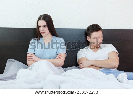 Portrait of unhappy and annoyed young caucasian couple after quarreling in bedroom under stress. Upset and angry man and woman sitting next to each other, relationship and marriage sex problems
