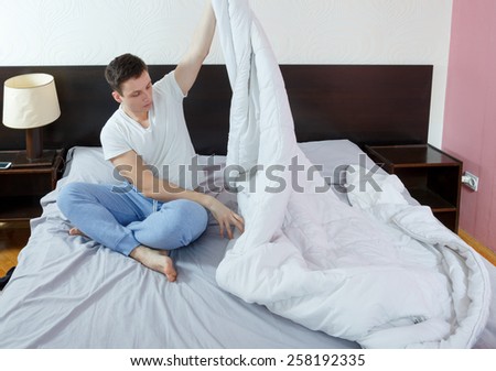 Young handsome man cleaning bed in morning. Housekkeping action