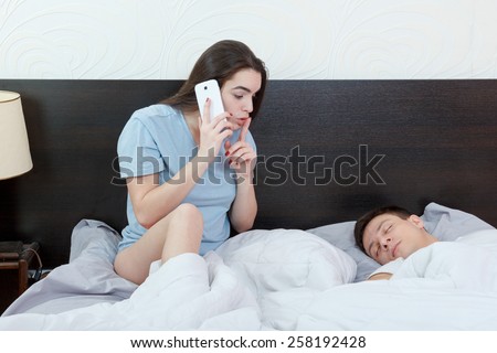 Young woman talking to phone with other while man is sleeping soundly in bedroom, cheating. Jealousy and suspicion in relationship. Problems in marriage, caucasian couple.