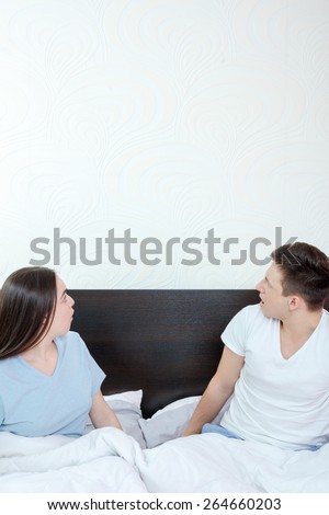 Handsome man and pretty surprised woman in bedroom looking up at thinking speech bubble, comic cloud or empty copyspace. Sexy young couple in bed, domestic atmosphere. Place for text and advertising