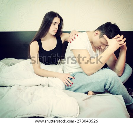 Depressed man sitting on edge of bed having problem against his woman. Young married couple who having problem in bed. Girl aspires and comforting sad man after an argument or quarrel. Money problem.