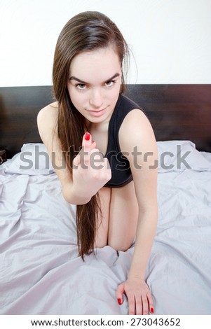 Beautiful young woman lying and waiting for you in the bed. Seductive pretty girl in black underwear evokes or calling out with finger a man to come into bedroom. Call for making love. Domestic photo.