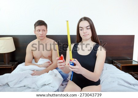Half-naked insecure and scared man posing while woman holding in  hands two meters and measuring desired length. Concept of smaller and larger sizes of male genitalia, comparison of expectations.