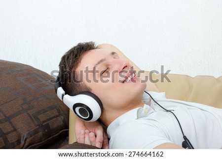 Handsome man with headset listening to music smiling lying on couch relaxing