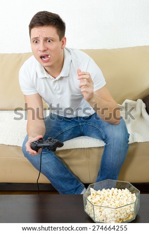 Guy eating popcorn with joystick for game console , Young man enjoying playing video game at home holding joystick with popcorn in mouth