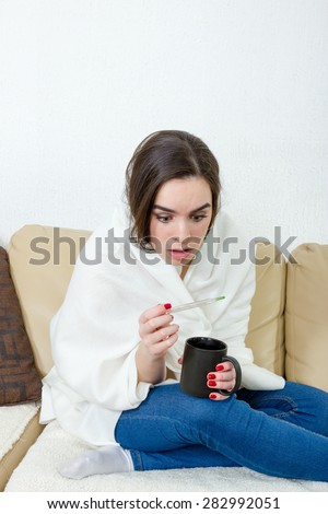 Upset woman with thermometer sick colds, flu, fever and migraine in bed with cup of tea or coffee. Girl with high temperature and headache virus. Female caught cold covered with white blanket at home.