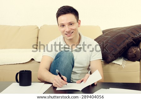 College student concentrating on studying sitting on living room floor with books and notes and pen. Home living lifestyle,  learning for exam concept. Handsome man with papers and cup of coffee.