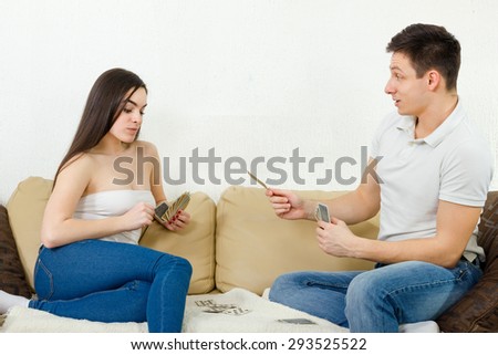 Beutiful couple playing cards indoor. Boyfriend explains game rules to his girlfriend. Couple afternoon relaxing on couch. Circumvention concept in gambling with cards