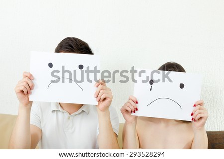 Sad young couple, young couple in despair.. Male and female with sad faces. Man and woman cover their faces with sad smile drawn on paper with one tear.