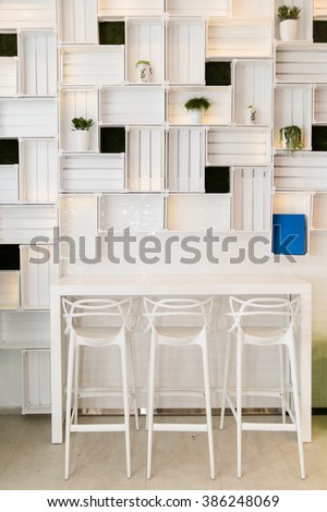 Bar Stools in Modern Caffe or Home Kitchen Wall. Nice Hotel Lounge Bar with White Three Barstool Seats and Shelfs, Table and Flowerpot with Green Plants. Minimalist Design, Domestic Atmosphere